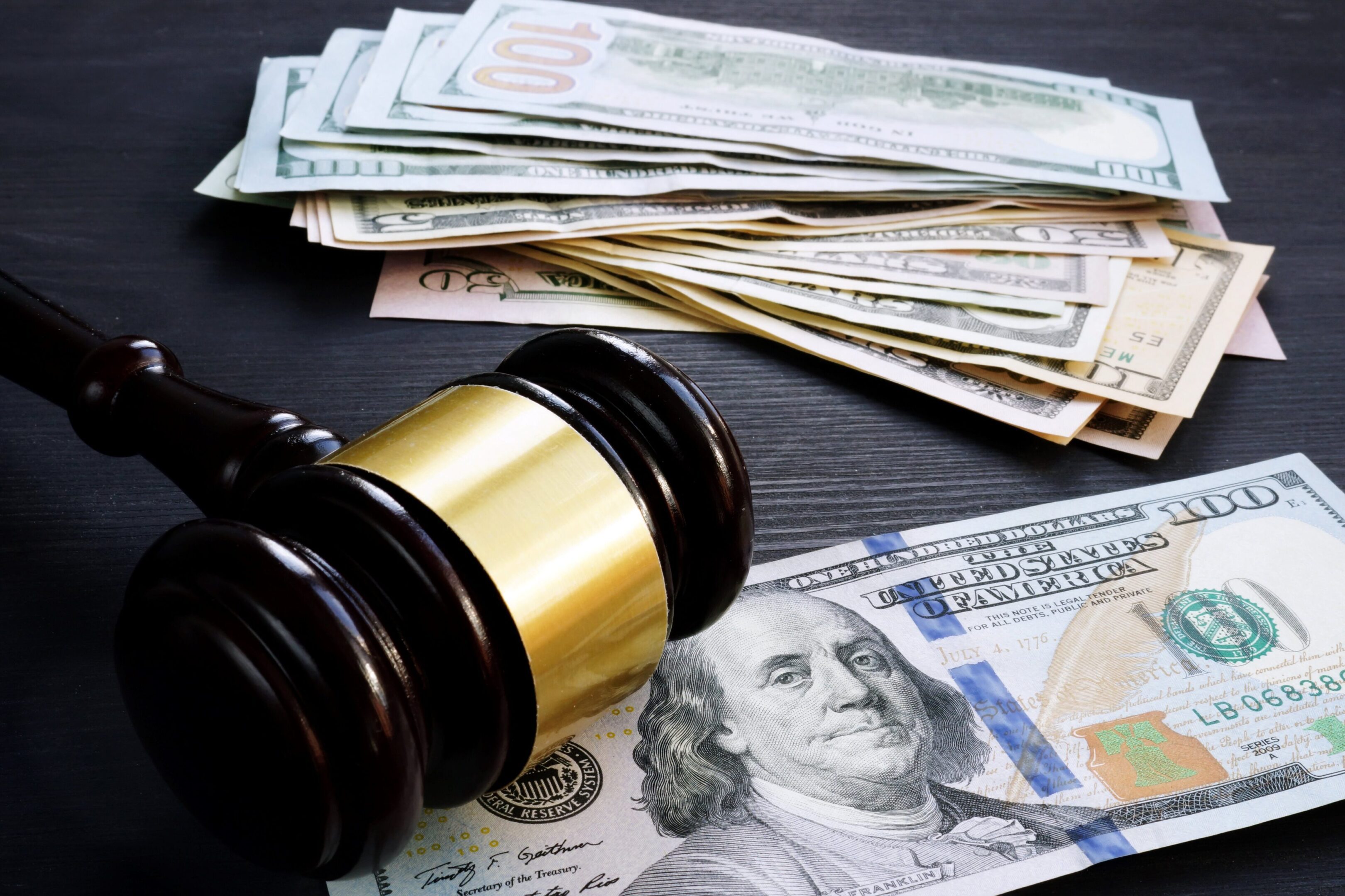 A gavel lies next to a stack of U.S. dollar bills.